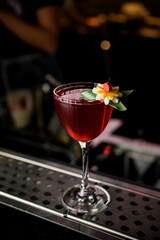 Red cocktail with slice of orange and orange zest in drinking glass on steel bar counter