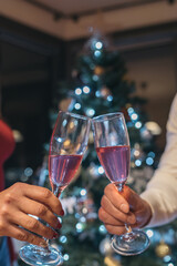Vertical image of the hands of a man and a woman toasting with their crystal glasses in front of the Christmas tree.