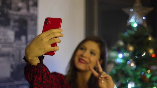 Young girl taking photos of herself in different poses in front of Christmas tree. Middle aged woman taking Christmas selfies at home.