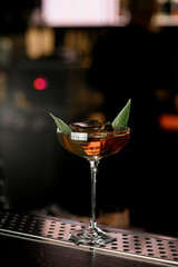 Selective focus on glass of delicious cocktail decorated with banana leaf and ice cube on steel barstand