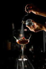 Bartender girl finishes making tasty cocktail and sprays it with transparent bitter