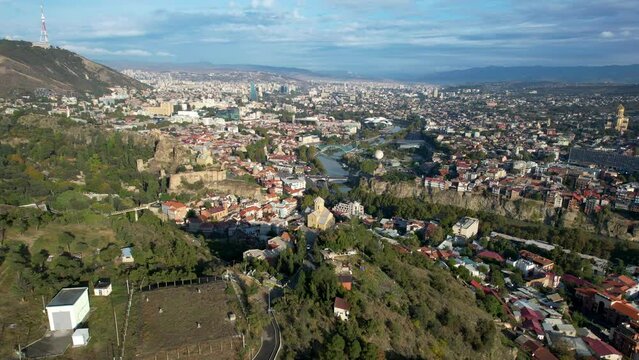 4k aerial tbilisi city footage just after sunrise with sun lights and blue clouds in the sky