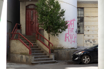 Tbilisi, Georgia - October 2, 2023: House with porch. White wall with text eat the rich. Car parking. Georgian courtyard. Train house with tree. Concept of rent apartment, mortgage, real estate agency - obrazy, fototapety, plakaty