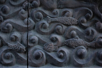 Fragment of gray stone bas-relief with fish in sea, ocean waves, river, water. Concept of wild life, sea animals, fishing, fisherman, art, religion, swimming, catching fish. Wall of house in Georgia - obrazy, fototapety, plakaty