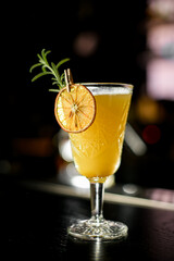 Selective focus of illuminated old-fashioned glass with warming yellow alcoholic cocktail on bar counter at dark bar
