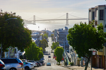 Sunny hilltop view of Oakland Bay Bridge from city street with oncoming car