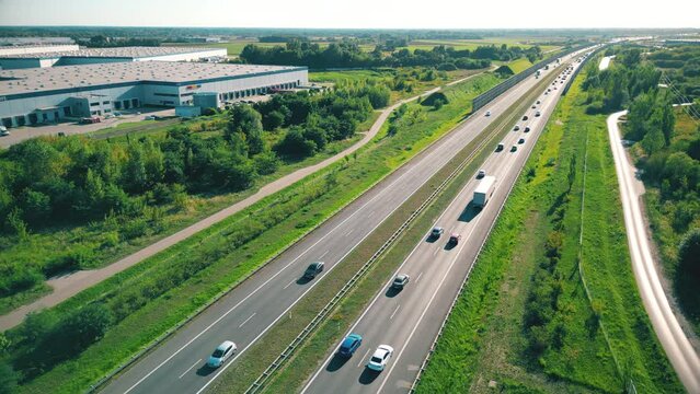 Aerial top view of highway road. Drone view of the elevated road, traffic junctions, and green garden. Transport trucks and cars driving on highway. Infrastructure in modern city.