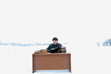 lonely man in a snowy field at a table reading a book, the concept of creativity, editorial work and the psychiatric disease schizophrenia.