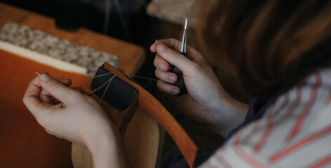 A leather craftswoman working, we see these hands sewing