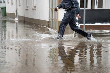 Policeman running through the water of a flooded street during high water of the river Trave in the old town of Lubeck at the Baltic sea in Germany, copy space - obrazy, fototapety, plakaty