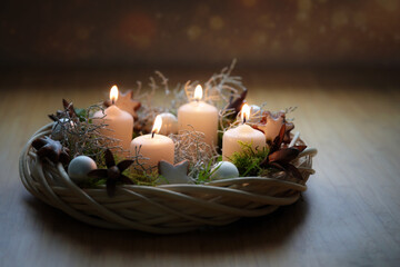 Advent wreath in natural tones made of wicker with beige candles, moss and Christmas decoration on a wooden table against a dark background, copy space, selected focus