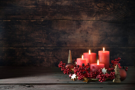Fourth advent with lighted red candles in a wreath of decoration berries, Christmas balls and cinnamon star cookies against a dark rustic background, copy space, selected focus