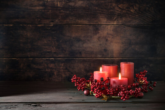 Second Advent with two lit red candles in a wreath from berries with Christmas decoration against a dark rustic wooden background, copy space, selected focus