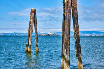 Pier remnants in San Francisco Bay framing Alcatraz Island with distant shoreline