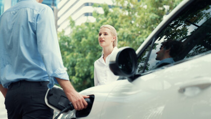 Progressive businessman and businesswoman install charger plug from charging station to electric...