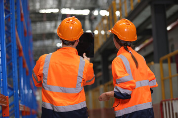 A couple of young logistic engineers wearing orange safety jackets and helmets work in the...