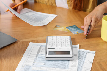 Woman with credit cards calculating taxes at wooden table, closeup