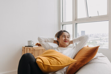 Happy asian woman sit and relax on bean bag in living room by the windows.