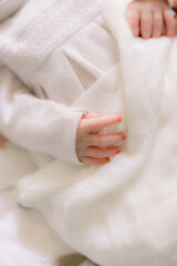 Adorable newborn baby hands. The baby girl wears a white dress and it's a close-up shot of her tiny hands. 