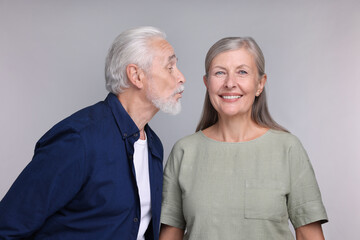 Senior man kissing his beloved woman on light grey background