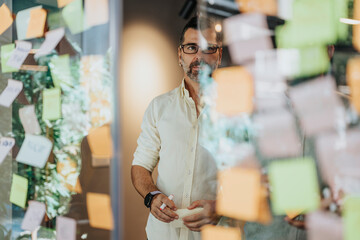 Diverse businesspeople brainstorming and collaborating in a modern office. Colorful sticky notes with statistics and project costs cover the glass wall.