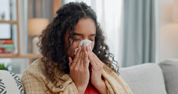 Allergies, sinus and sick woman sneezing on a sofa with tissue paper for nasal, cleaning or virus at home. Flu, stress and female blowing nose in living room with viral infection, bacteria or covid