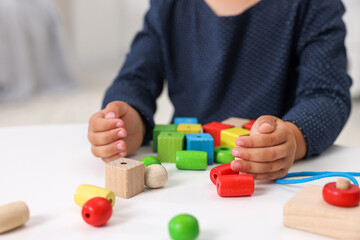 Fototapeta premium Motor skills development. Little girl playing with wooden pieces and string for threading activity at table, closeup