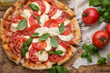 Delicious Caprese pizza with tomatoes, mozzarella and basil on wooden table, flat lay