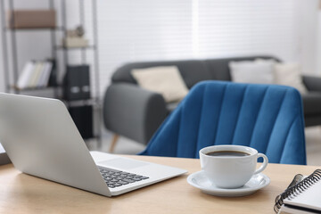 Home workspace. Laptop, cup of coffee and stationery on wooden desk indoors