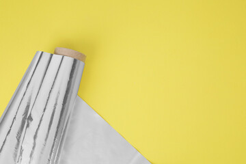 Roll of aluminum foil on yellow background, top view. Space for text