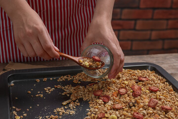 Woman putting granola from baking tray into jar at table, closeup