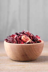 Dry hibiscus tea in bowl on wooden table, space for text