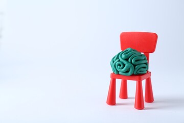 Brain made of plasticine on mini chair against white background. Space for text