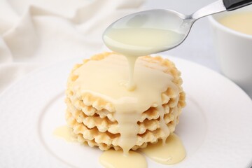 Pouring tasty condensed milk onto waffles on table, closeup