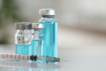 Glass vials with light blue medication and syringe on white table, closeup. Space for text