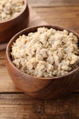 Tasty boiled oatmeal in bowl on wooden table, closeup