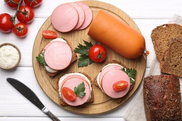 Delicious sandwiches with boiled sausage, tomato and sauce on white wooden table, flat lay