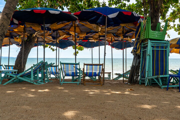 On the seashore there are sun loungers and blue umbrellas against the background of the sky with clouds. Umbrellas are inserted into the sand of a sandy beach.