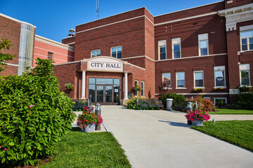 Sidewalk with pink flowers in pots leading to public city hall entrance