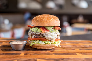 Double bacon cheeseburger and mayonnaise  with close-up view on wooden board with blurred background