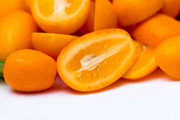 Multiple kumquats on a white background with one cut in half