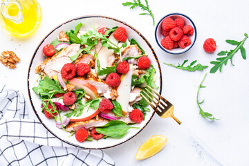 Fresh salad with raspberries, grilled chicken, pears, cheese, onion, walnuts, spinach and arugula, white table background, top view