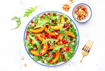 Vegan autumn salad with baked sweet pumpkin, lettuce, arugula, pomegranate seeds and walnuts. Comfort slow  food. White table background. Top view