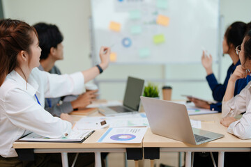 portrait of young asian business team presents business profits to colleagues at meeting, explaining business turn over on flipchart to coworkers in office with using tablet.