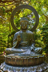 Buddha statue with palm raised and green nature garden behind it