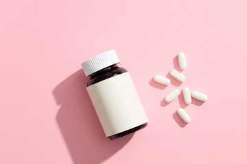 An unlabeled medicine bottle, accompanied by several white pills on a pink background. The...