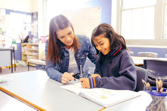 Aboriginal female school teacher sitting with her student in the classroom - Powered by Adobe