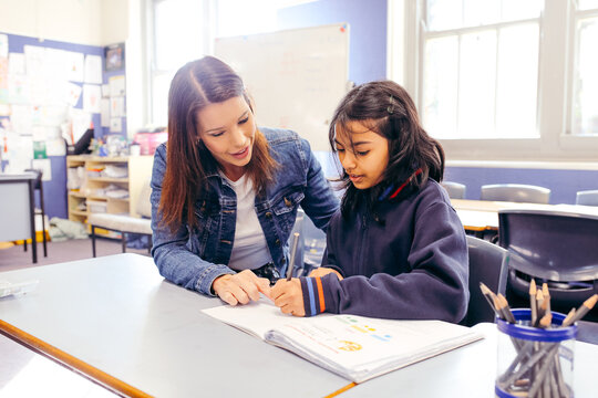 Aboriginal female school teacher sitting with her student in the classroom