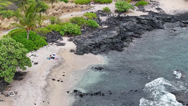 Aerial woman sunbathing beautiful beach surf lava. Blue Pacific ocean water. Snorkel and scuba dive vacation destination. Black volcanic lava rock. Recreation and relaxation. Tropical landscape.