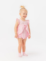 A happy 2-year-old toddler girl in a pink dress laughs on a white background. It stands sideways.